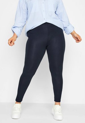 Marineblauwe leggings van rekbaar, glad materiaal, met een aansluitend ontwerp en een enkel-lange snit, gecombineerd met een lichtblauw gestreept shirt en witte sneakers.