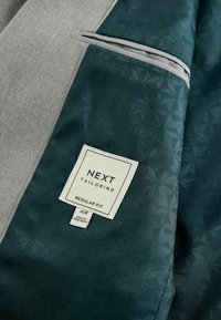 Next Tailoring suit jacket interior features a gray textured fabric and a dark green patterned lining. Includes a label with size and care details.