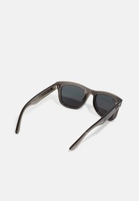 Ochelari de soare cu un cadru gri transparent, lentile întunecate și brațe elegante. Prezintă o strălucire subtilă și o formă pătrată modernă.