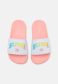 Rozā slīdēšanas sandales ar baltu siksnu, uz kuras ir daudzkrāsains "HILFIGER" teksts un logo. Teksturēta zole labākai saķerei.