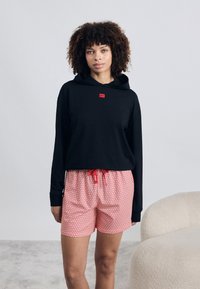 Zwarte hoodie met een klein rood logo, gecombineerd met rode gestreepte shorts met een koord en een elastische tailleband.