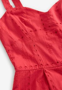 Tessuto rosso ricamato con spalline regolabili, caratterizzato da motivi floreali e dettagli a intaglio, creando un aspetto testurizzato.