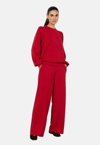 Röda, löst sittande sweatpants och matchande tröja. Tröjan har puffärmar medan byxorna har sidofickor. Mjukt material, minimal design.