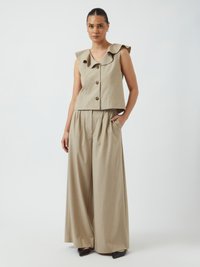 Beige ermeløs topp med volangkant og frontknapper, kombinert med vide beige bukser. Glatt tekstur; minimalistisk design.