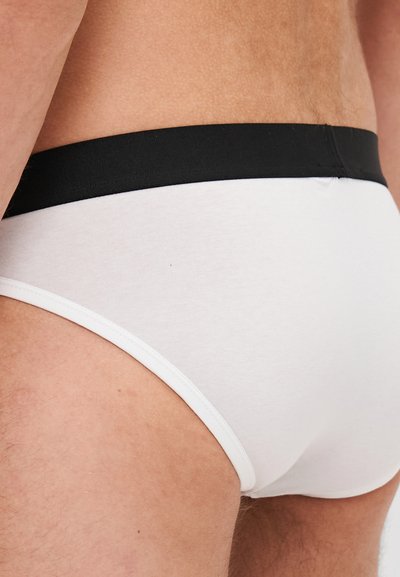 Culottes en coton blanc avec une ceinture élastique noire, présentant une texture lisse et un design ajusté, montrant la vue de dos et de côté.