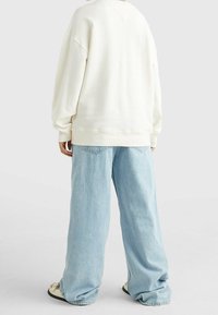 Felpa crema con spalle abbassate, polsini e orlo a coste, abbinata a jeans chiari, larghi con tasche posteriori.