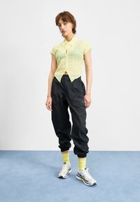 Camisa de botón corta de manga corta de un amarillo claro y texturizado, combinada con pantalones negros sueltos y zapatillas blancas, complementada con calcetines amarillos brillantes.