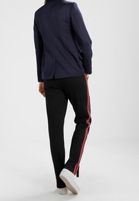 Námořnický blazer s přizpůsobeným střihem a rozparkem vzadu, kombinovaný s černými kalhotami s červenými pruhy po stranách a bílými teniskami. Jednoduchý a moderní design.