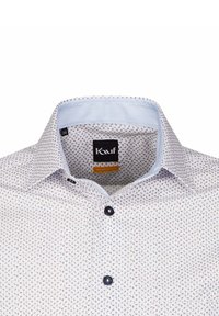 Camicia bianca con un piccolo motivo blu ripetitivo. Presenta un colletto classico, bottoni scuri e una fodera del colletto interno di un blu chiaro. Etichetta del marchio visibile.