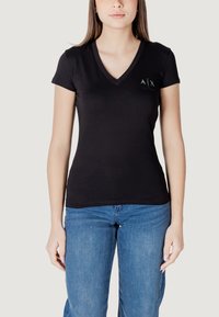 Maglietta nera a maniche corte con scollo a V realizzata in cotone morbido, con un piccolo logo sul lato sinistro e un design aderente. Abbinata a jeans blu.