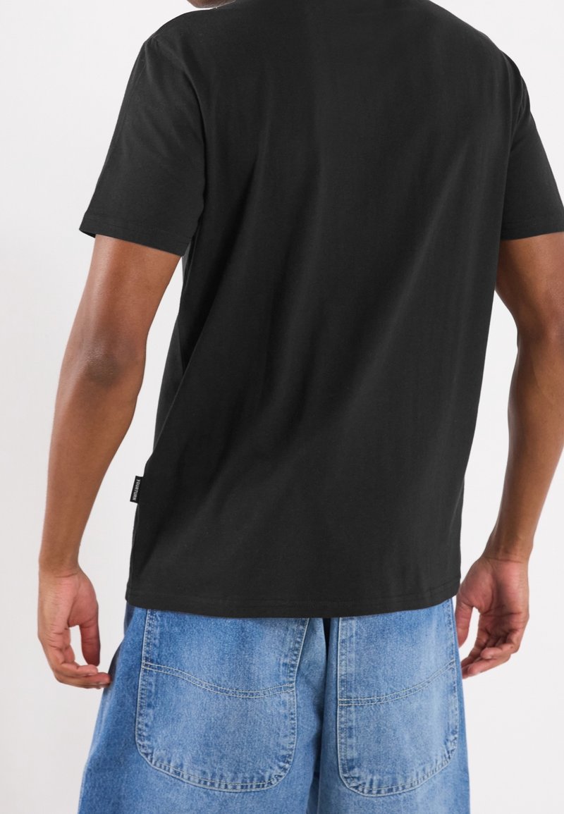 Sort bomulds T-shirt med korte ærmer, rund halsudskæring og mærkedetalje ved kanten, parret med blå denimshorts med store lommer.