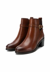 Par de botas de cuero marrón lisas hasta el tobillo con tacones de bloque y una correa decorativa con una hebilla dorada en el lado exterior.