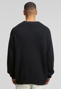 Maglione nero a maglia con texture a coste, scollatura rotonda e spalle basse. Le maniche e l'orlo presentano una finitura a coste larga.