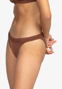 Bas de bikini marron au design simple, avec une taille élastique douce et une couverture minimale. Texture lisse avec de légères marques d'étirement visibles.