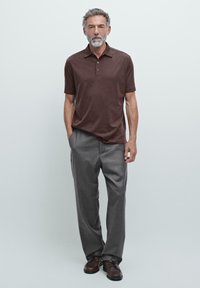 Brun kortærmet polo skjorte, grå skræddersyede bukser, brune sko. Pasformen er løs, og stoffet ser glat og let ud.