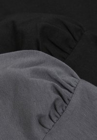 Två tygstycken: ett svart och ett mörkgrått. Båda är ribbade med en rynkad textur och överlappar något för synlighet.