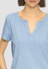 Lichtblauwe katoenen V-hals t-shirt met korte mouwen en een ontspannen pasvorm. De halslijn heeft een ruwe randdetail met een subtiele textuur.