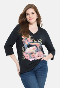 Top nero con maniche 3/4 caratterizzato da un design floreale colorato e una grafica di una macchina da cucire vintage sulla parte anteriore. Tessuto morbido, vestibilità comoda.