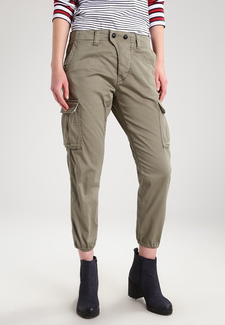 Olivgrüne Cargo-Hosen aus Baumwolle mit seitlichen Taschen, elastischen Bündchen und einer lockeren Passform. Getragen mit dunkelbraunen Knöchelstiefeln.
