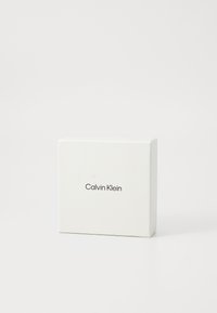 Calvin Klein gave eske; firkantet form, hvitt pappmateriale, forsiden har merkets navn i svart sans-serif skrifttype.