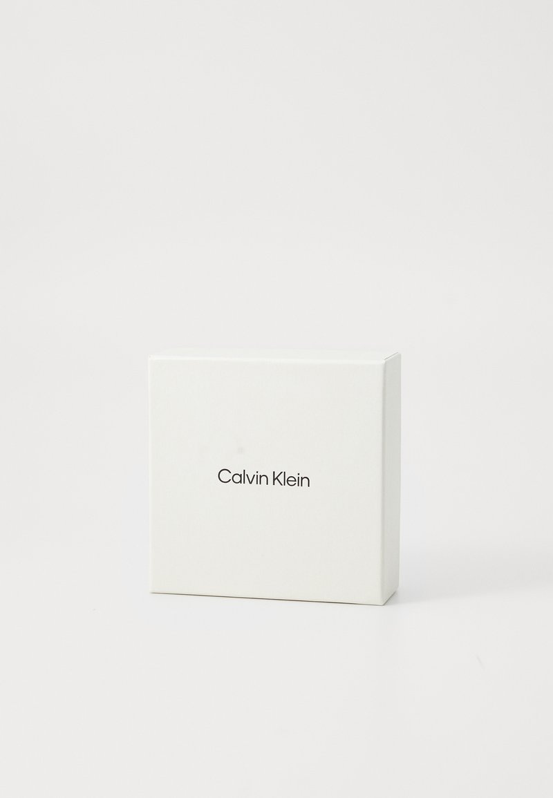 Boîte cadeau Calvin Klein ; forme carrée, en carton blanc, le devant présente le nom de la marque en police sans-serif noire.
