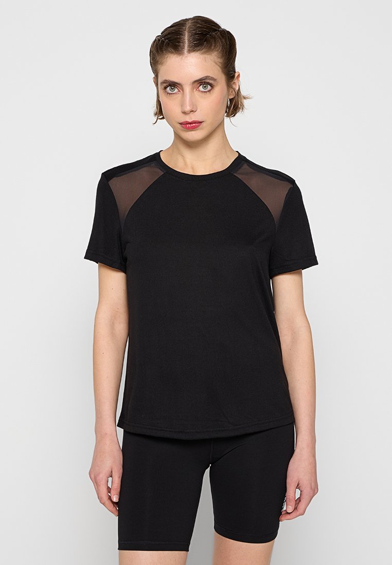 Camiseta atlética negra de manga corta, con paneles de malla en los hombros, escote redondo y un ajuste relajado. Combinada con pantalones cortos negros ajustados.