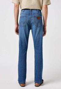 Jeans in denim blu con taglio dritto, dotati di due tasche posteriori con un motivo di cucitura decorativa e una patch in pelle con il marchio sulla vita.