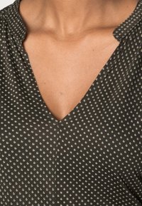 Black v-neck blouse featuring small white polka dots. The fabric is smooth, with a slight sheen and subtle stitching detail along the neckline.