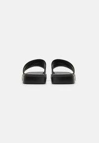 Sandale negre cu talpă plată, cu două curele curbate și o textură netedă. Design minimalist, fără hardware sau modele vizibile.