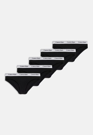 Cinq slips noirs Calvin Klein avec des ceintures blanches portant le logo Calvin Klein, disposés en diagonale sur un fond blanc.