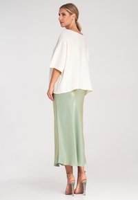 Lässiges, weißes Oberteil mit einem runden Ausschnitt, kombiniert mit einem glänzenden, knielangen Rock in Mintgrün. Transparente High-Heelsandalen vervollständigen den Look.