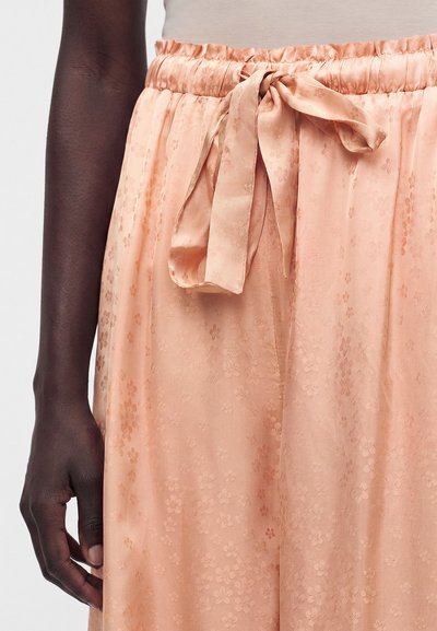 Παντελόνι από σατέν χρώματος ροδάκινο με λουλουδένιο ζακάρ σχέδιο και δεμένη κορδέλα στη ελαστική μέση, φορεμένο από άτομο με σκουρόχρωμο τόνο δέρματος.