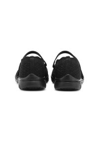 Pár černých pletených slip-on bot s elastickými patními popruhy a texturovanými gumovými podrážkami, zobrazených ze zadní strany na bílém pozadí.