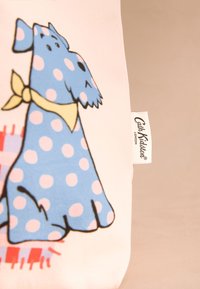 Mėlynas šuo su taškeliais, iliustruotas ant rožinės audinio fono, su geltonu kaspinu ir matomu "Cath Kidston" ženklu.