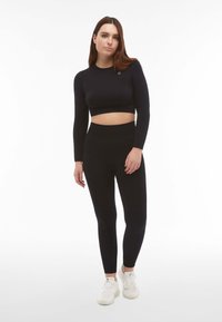 Top corto nero con maniche lunghe e leggings a vita alta, realizzati in tessuto elasticizzato. Abbinato a sneaker sportive bianche.