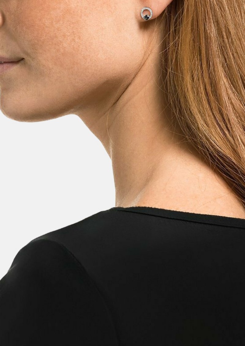 Silberne Ohrringe mit rundem Design, featuring einem dunklen zentralen Stein, umgeben von einem funkeltenden Rand, getragen von einer Person mit langen Haaren.