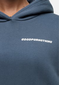 Felpa blu in cotone con una texture liscia, caratterizzata da una grafica testuale bianca ad arco verso l'alto: "GOODFORNOTHING" sul petto.