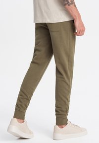 Olijfgroene joggers met een slim fit, geribde boorden, zijzakken en een zachte textuur, gecombineerd met lichtbeige sneakers.