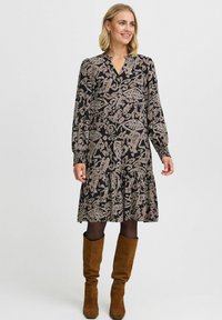 Rochie neagră cu mâneci lungi, decolteu în V și model floral în bej. Fustă evazată, material texturat, asortată cu cizme din suede, până la genunchi, de culoare maro.