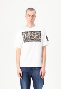 White short-sleeve t-shirt with a large black graphic logo in the center. Soft cotton material, relaxed fit, and round neck design.