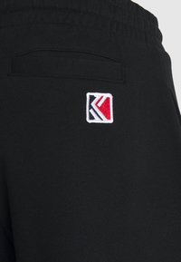 Black sweatpants featuring a back pocket and a multicolored embroidered logo with red, white, and blue elements. Soft cotton material.
