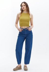 Top corto de mostaza de canalé, jeans azules de tiro alto y zapatos de plataforma beige, presentando un ajuste relajado con una textura suave.