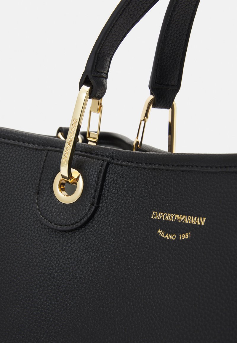 Borsa a mano in pelle nera con superficie texturizzata, hardware dorato, doppie maniglie e dettaglio del marchio impressa.
