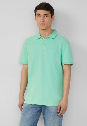 Polo-Shirt in hellmintgrün, mit kurzen Ärmeln, Kragen und drei Knöpfen, kombiniert mit hellblauen Jeans. Glatte Textur, lässiges Design.