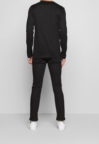Long-sleeve black shirt with a round neckline, paired with black pants and white sneakers. Smooth texture, simple design, no visible patterns.