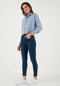 Blue and white striped button-up shirt, high-waisted dark denim skinny jeans, and white sneakers. Simple and fitted design.
