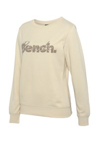Beige sweatshirt van zacht materiaal met lange mouwen. Heeft een groot metallic "Bench."-logo op de voorkant en ribgebreide boorden en een zoom.