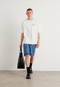 Balta trumpa rankovė T-marškiniai su "Calvin Klein" logotipu, mėlynos džinsinės šortai, juodos kojinės, juodi batai ir juoda rankinė. Minimalistinis dizainas.