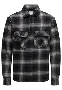 Camisa de cuadros en blanco y negro hecha de franela; presenta dos bolsillos en el pecho, un cuello y cierre de botones; mangas largas con puños abotonados.