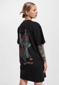 Must musta oversized T-särk, mille seljal on graafiline kujundus rooside ja nuga. Lühikesed varrukad ja mugav lõige.